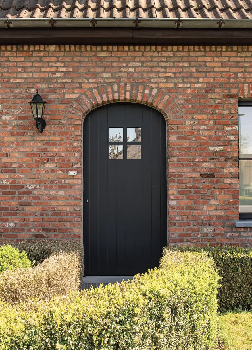 Zwarte PVC boogdeur met glasverdeling in een gerenoveerde hoevegevel